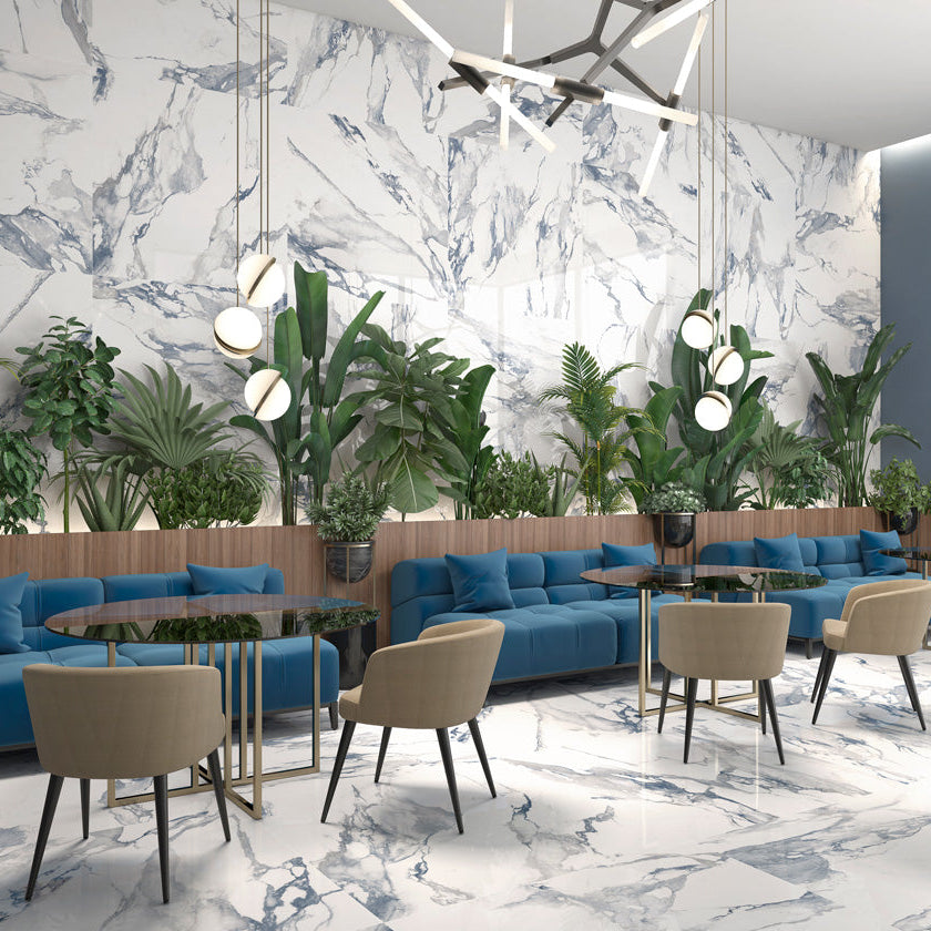 Modern interior with blue sofas, beige chairs, and decorative plants against a marble wall.