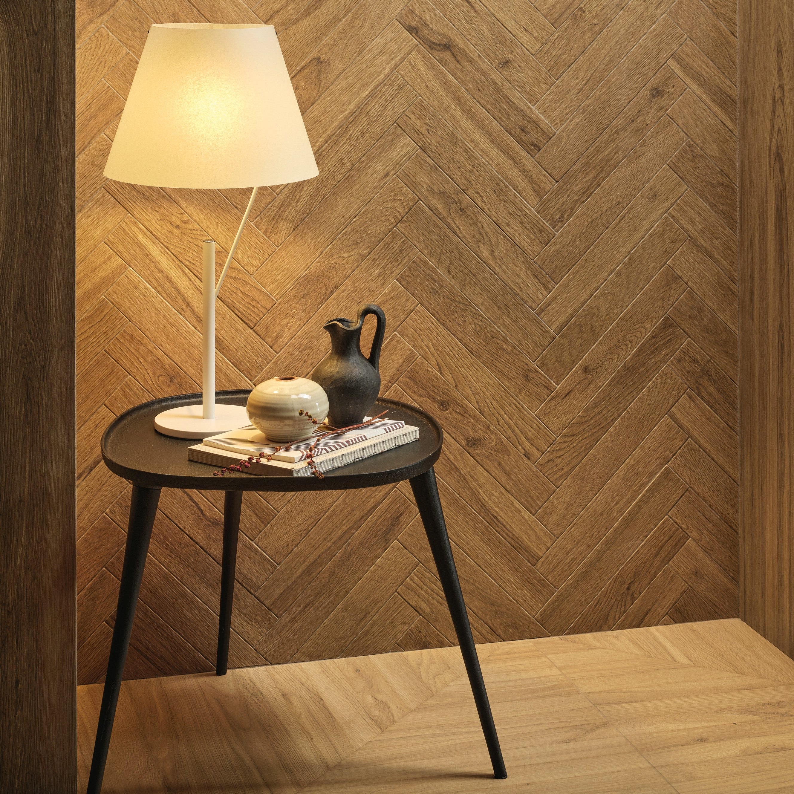 Small round table with a lamp and decorative items against a wooden chevron wall.