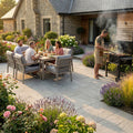 People enjoying a meal outdoors in a garden setting with a man grilling.